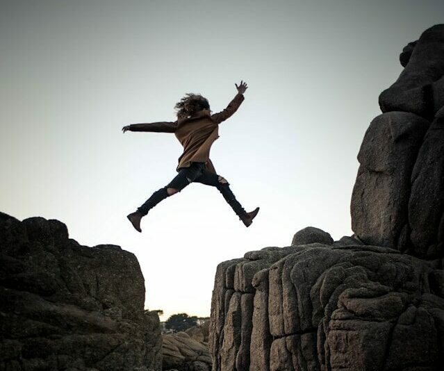 Foto van Micah Sammie - meisje dat over een kloof springt tussen rotsen. Ze lijkt op Ronja de Roversdochter.
